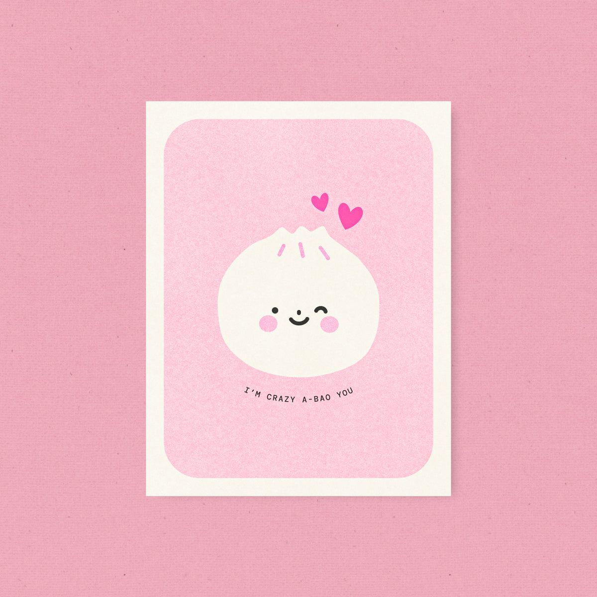 Whimsical Asian food-inspired risograph love card printed with yellow vegetable-based ink, featuring a cute winking dumpling bao bun with rosy cheeks and two little hearts. The words "I'm Crazy A-Bao You" curve beneath it, and a kraft envelope is included. A delightful handmade card from Seattle, WA by Minna May.