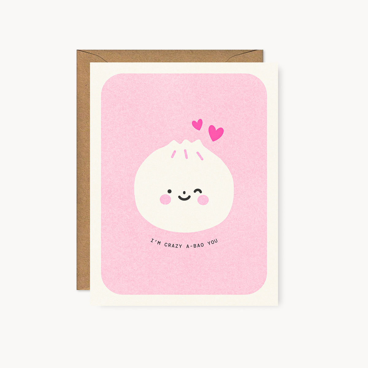 Whimsical Asian food-inspired risograph love card printed with yellow vegetable-based ink, featuring a cute winking dumpling bao bun with rosy cheeks and two little hearts. The words "I'm Crazy A-Bao You" curve beneath it, and a kraft envelope is included. A delightful handmade card from Seattle, WA by Minna May.