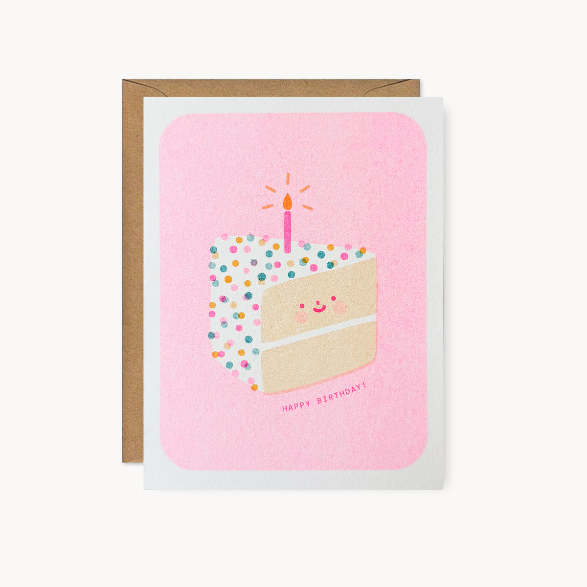 Whimsical risograph birthday card printed with fluorescent pink, yellow, and teal vegetable-based inks, featuring a cute smiling slice of confetti cake with rosy cheeks and a single glowing candle on a pink background. The words "Happy Birthday!" appear beneath it, and a kraft envelope is included. A delightful handmade card from Seattle, WA by Minna May.