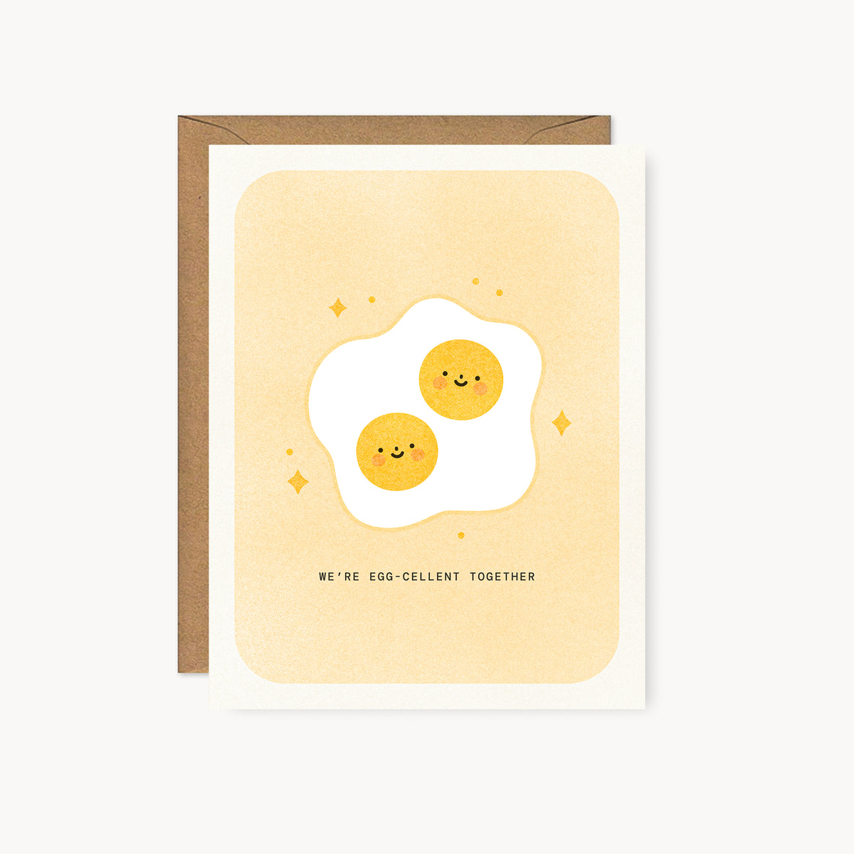 Whimsical risograph love card printed with yellow vegetable-based ink, featuring a cute fried sunny side up egg with two smiling yolks and rosy cheeks, surrounded by little sparkles. The words "We're Egg-cellent Together" appear below, and a kraft envelope is included. A delightful handmade card from Seattle, WA by Minna May.