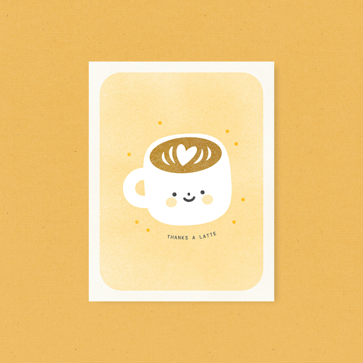 Whimsical risograph thank you card printed with yellow vegetable-based inks, featuring a cute smiling latte mug filled with coffee with a heart latte art on a yellow background. The words "Thanks a latte" curve beneath it, and a kraft envelope is included. A delightful handmade card from Seattle, WA by Minna May.